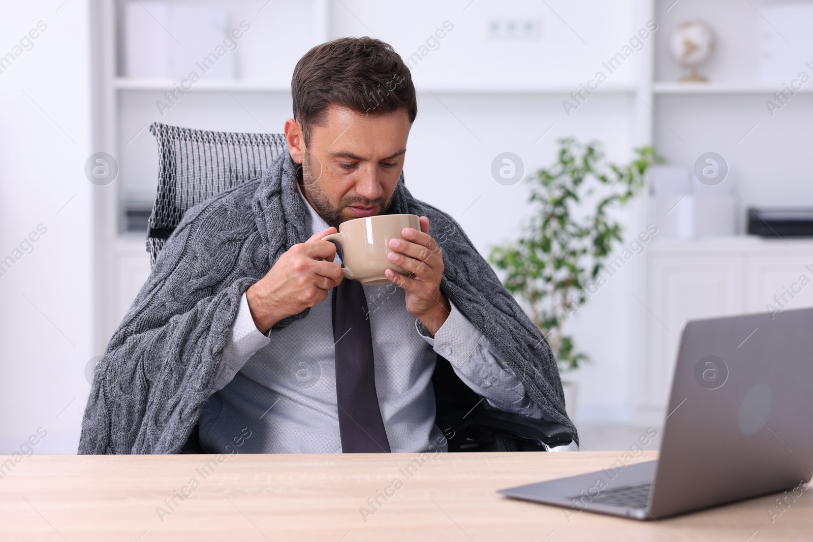 Photo of Air conditioning. Man with cup of hot drink suffering from cold temperature at workplace in office