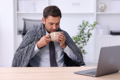 Photo of Air conditioning. Man with cup of hot drink suffering from cold temperature at workplace in office