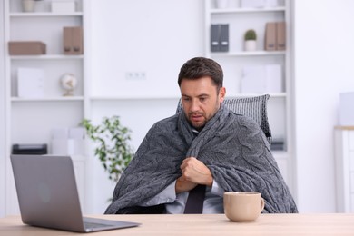 Photo of Air conditioning. Man with blanket suffering from cold temperature at workplace in office