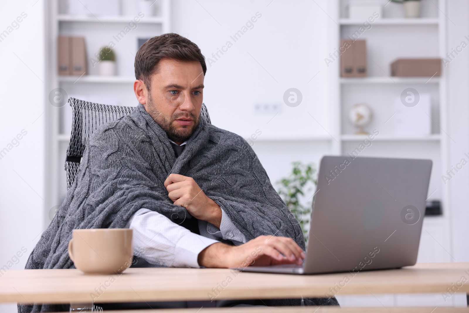 Photo of Air conditioning. Man with blanket suffering from cold temperature at workplace in office