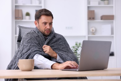Photo of Air conditioning. Man with blanket suffering from cold temperature at workplace in office