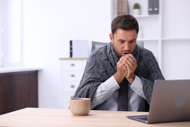 Photo of Air conditioning. Man with blanket suffering from cold temperature at workplace in office