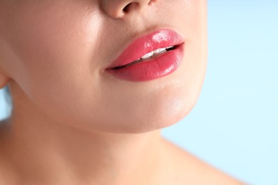 Photo of Woman with beautiful pink lipstick on her lips against light blue background, macro view