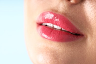 Photo of Woman with beautiful pink lipstick on her lips against light blue background, macro view