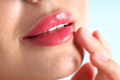Photo of Woman with beautiful pink lipstick on her lips against light blue background, macro view