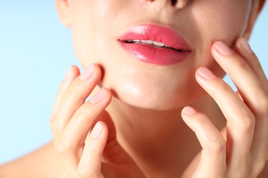 Photo of Woman with beautiful pink lipstick on her lips against light blue background, macro view