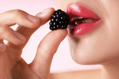 Photo of Woman with beautiful lipstick on her lips and blackberry against pink background, macro view