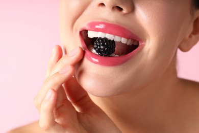 Photo of Woman with beautiful lipstick on her lips and blackberry against pink background, macro view