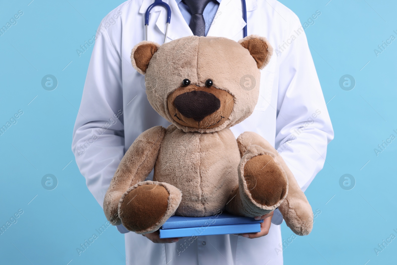 Photo of Pediatrician with teddy bear and notebooks on light blue background, closeup