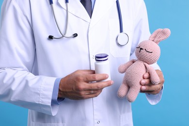 Photo of Pediatrician with toy bunny and pills on light blue background, closeup