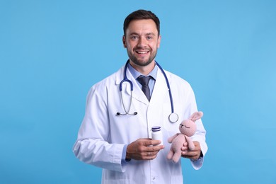 Photo of Pediatrician with toy bunny and pills on light blue background