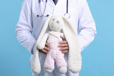 Photo of Pediatrician with toy bunny on light blue background, closeup