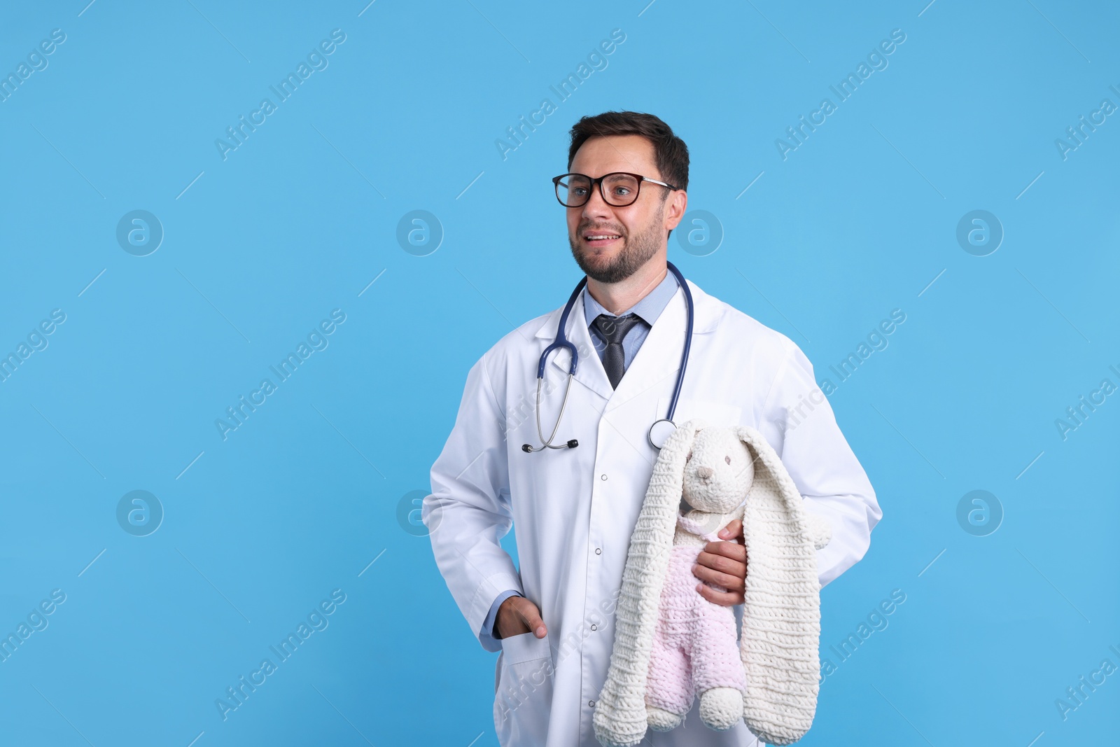 Photo of Pediatrician with toy bunny on light blue background. Space for text