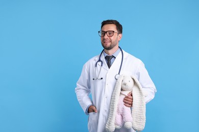 Photo of Pediatrician with toy bunny on light blue background. Space for text