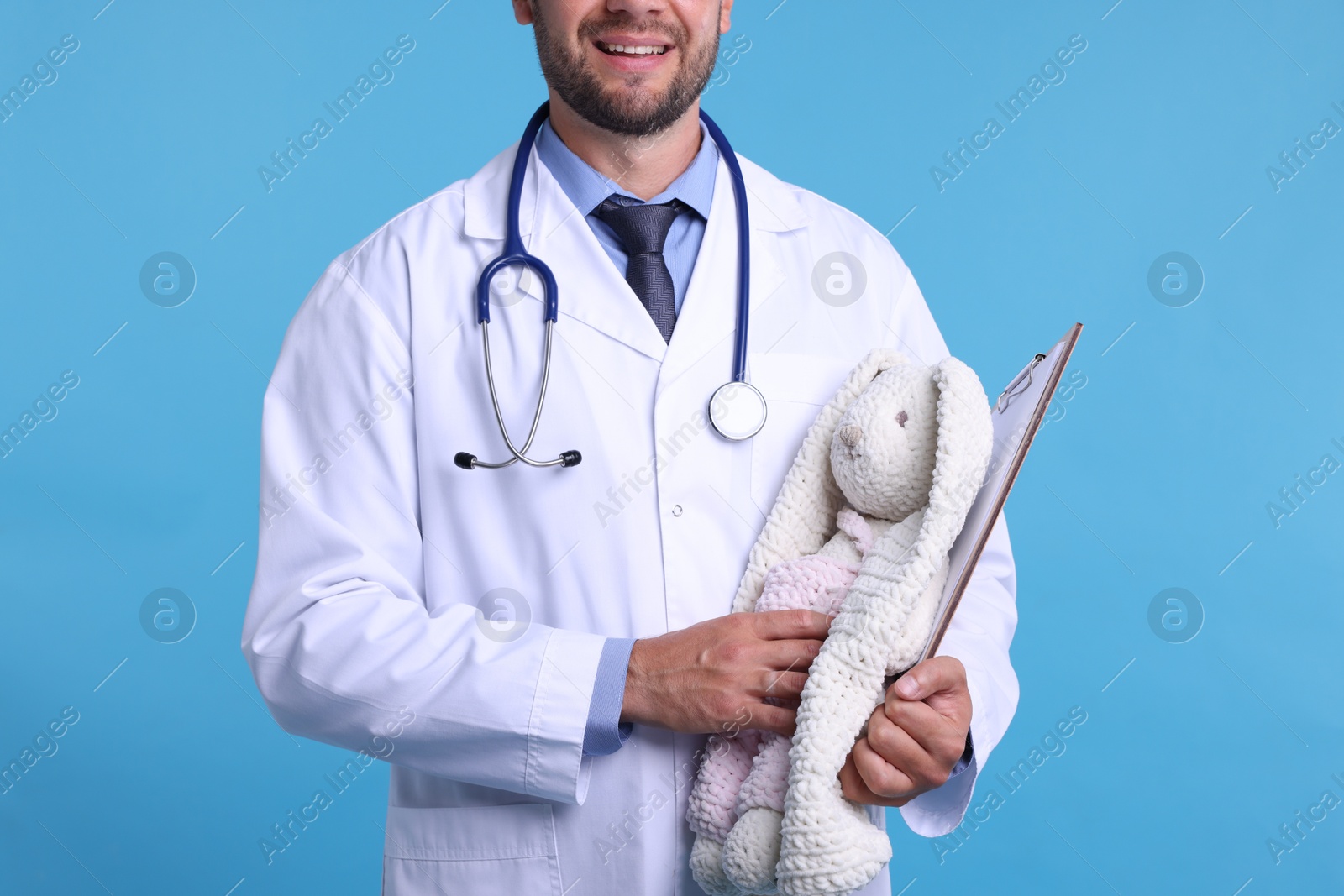 Photo of Pediatrician with toy bunny and clipboard on light blue background, closeup