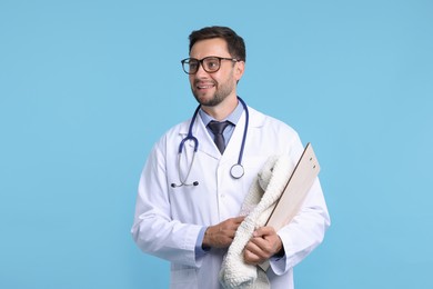 Photo of Pediatrician with toy bunny and clipboard on light blue background
