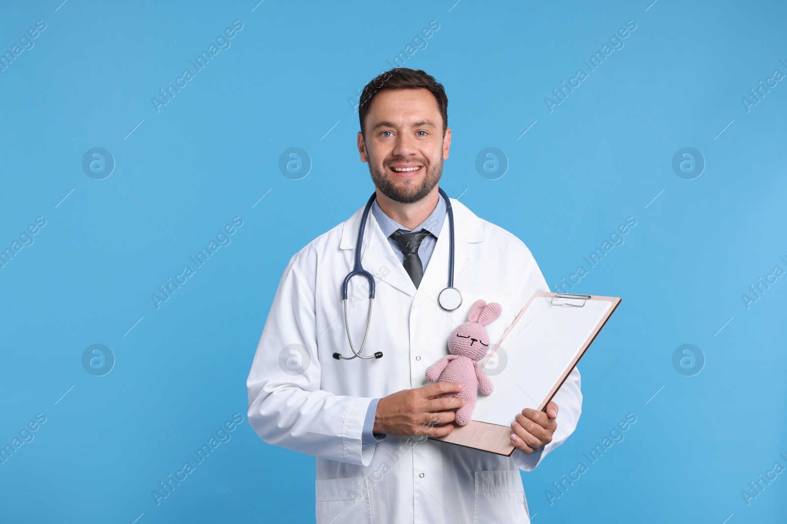 Photo of Pediatrician with clipboard and toy bunny on light blue background