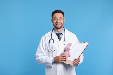 Photo of Pediatrician with clipboard and toy bunny on light blue background