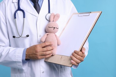 Photo of Pediatrician with clipboard and toy bunny on light blue background, closeup