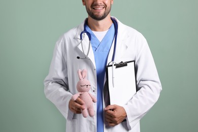 Photo of Pediatrician with clipboard and toy bunny on green background