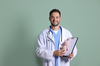 Photo of Pediatrician with clipboard and toy bunny on green background. Space for text