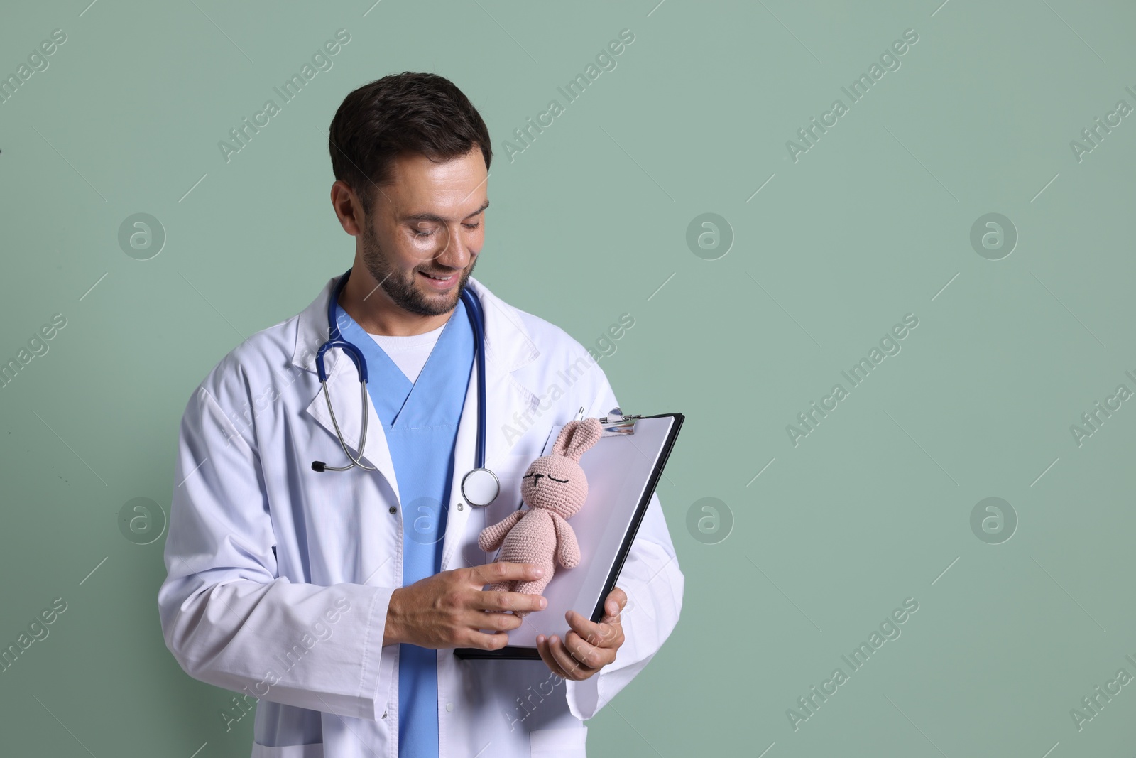 Photo of Pediatrician with clipboard and toy bunny on green background. Space for text