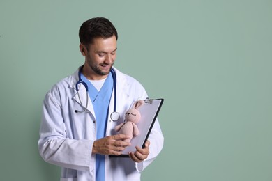 Photo of Pediatrician with clipboard and toy bunny on green background. Space for text