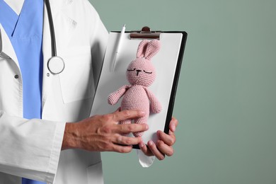 Photo of Pediatrician with clipboard and toy bunny on green background, closeup. Space for text