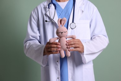 Photo of Pediatrician with toy bunny on green background, closeup