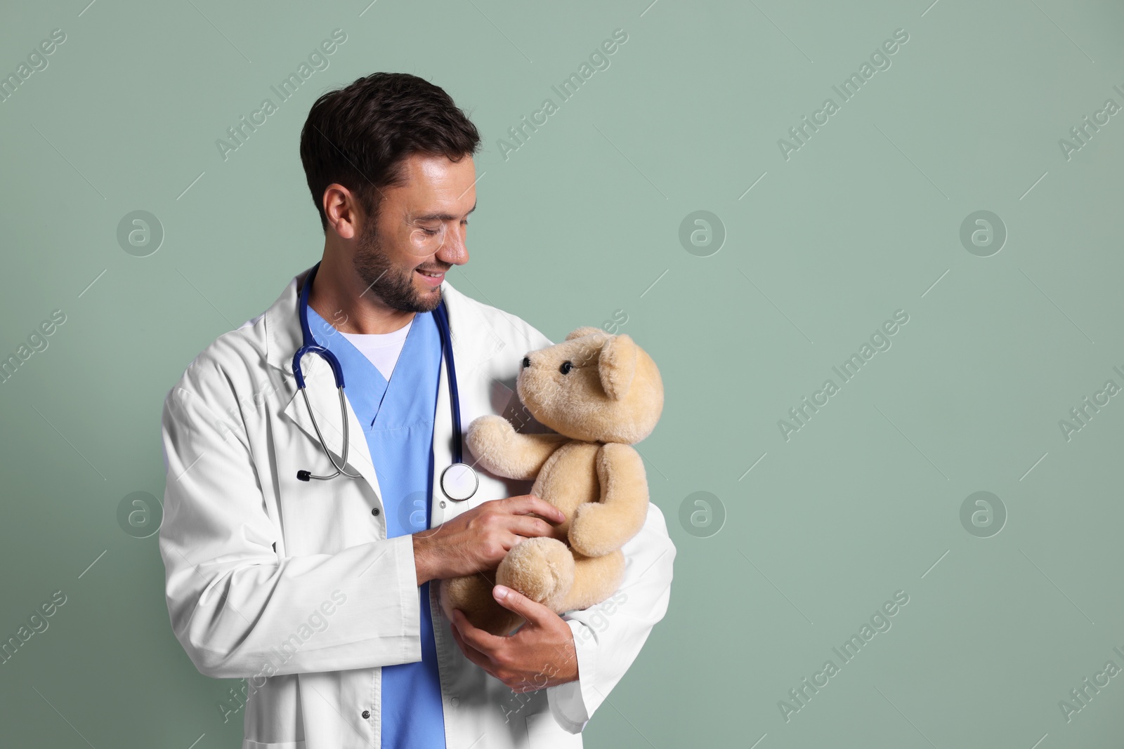 Photo of Pediatrician with teddy bear on green background. Space for text