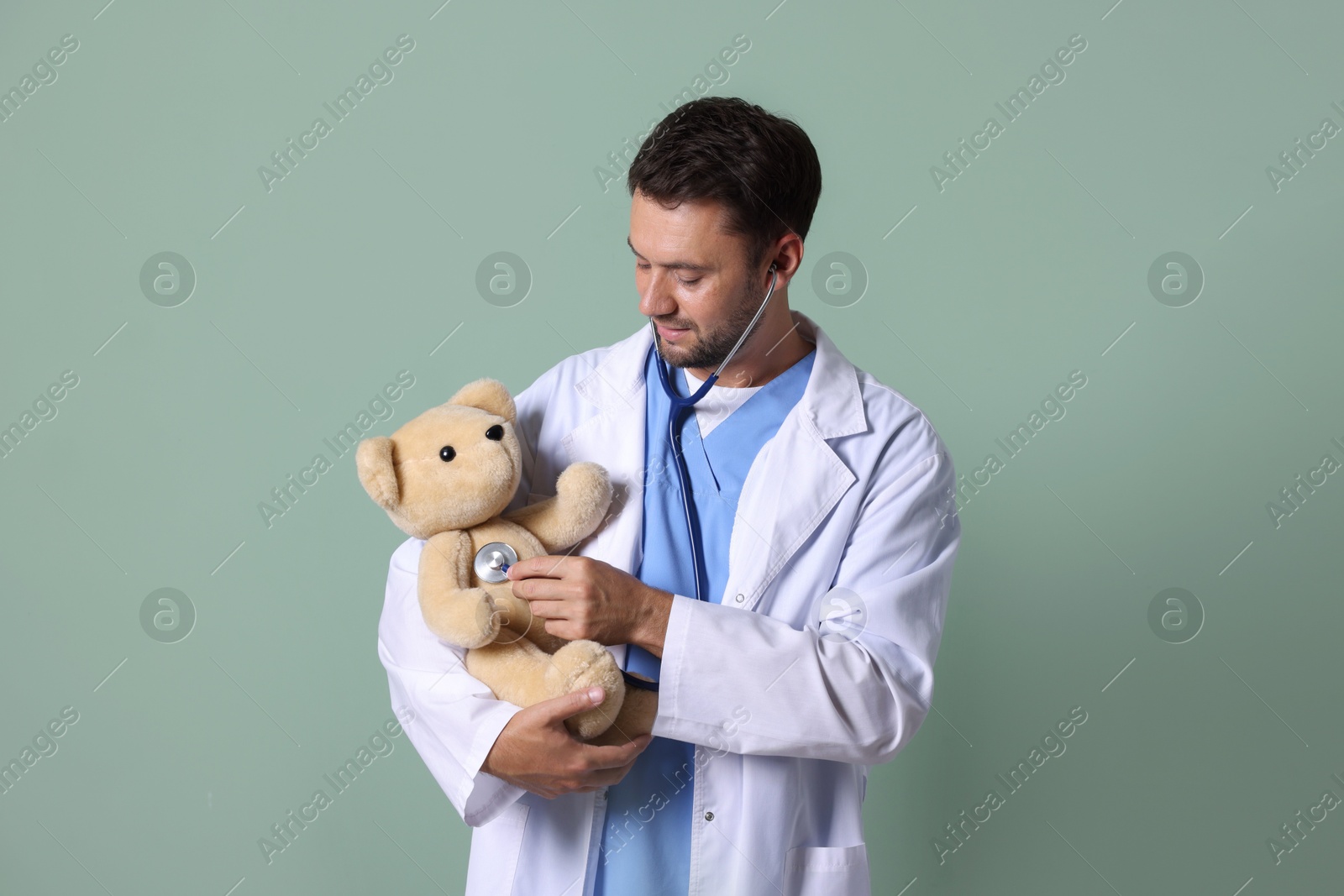 Photo of Pediatrician checking heartbeat of teddy bear on green background