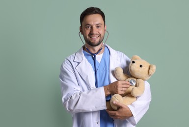Photo of Pediatrician checking heartbeat of teddy bear on green background