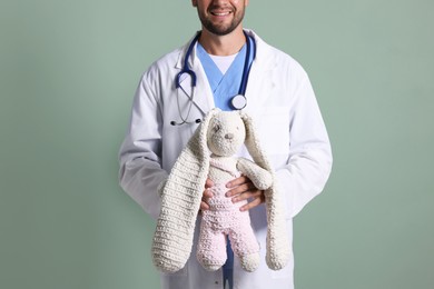 Photo of Pediatrician with toy bunny on green background, closeup