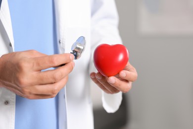 Photo of Pediatrician with stethoscope and heart model in hospital, closeup. Space for text