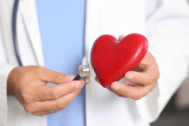 Photo of Pediatrician with stethoscope and heart model in hospital, closeup