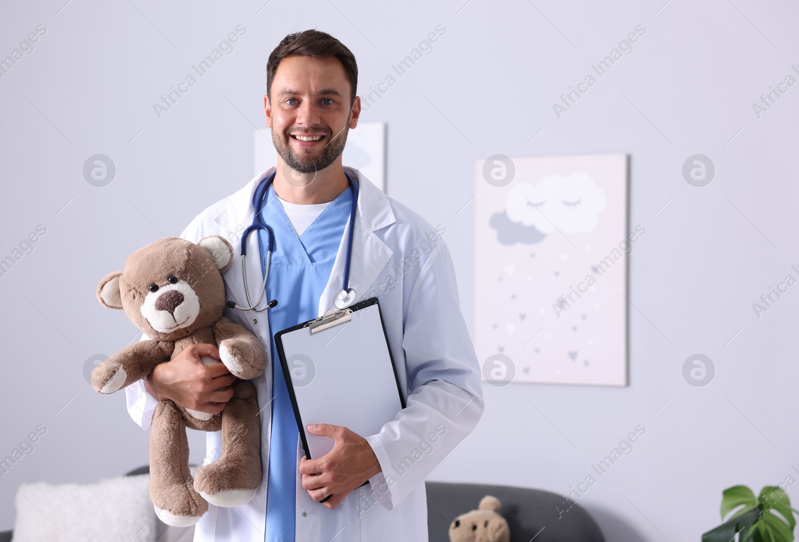 Photo of Pediatrician with teddy bear and clipboard in hospital. Space for text