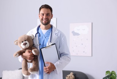 Photo of Pediatrician with teddy bear and clipboard in hospital. Space for text