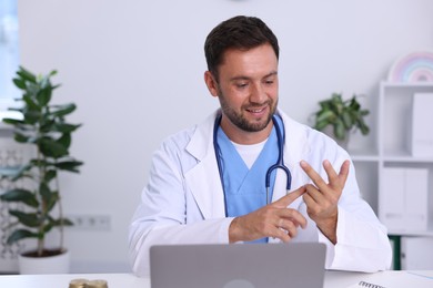 Photo of Pediatrician having video call with patient via laptop at desk in hospital