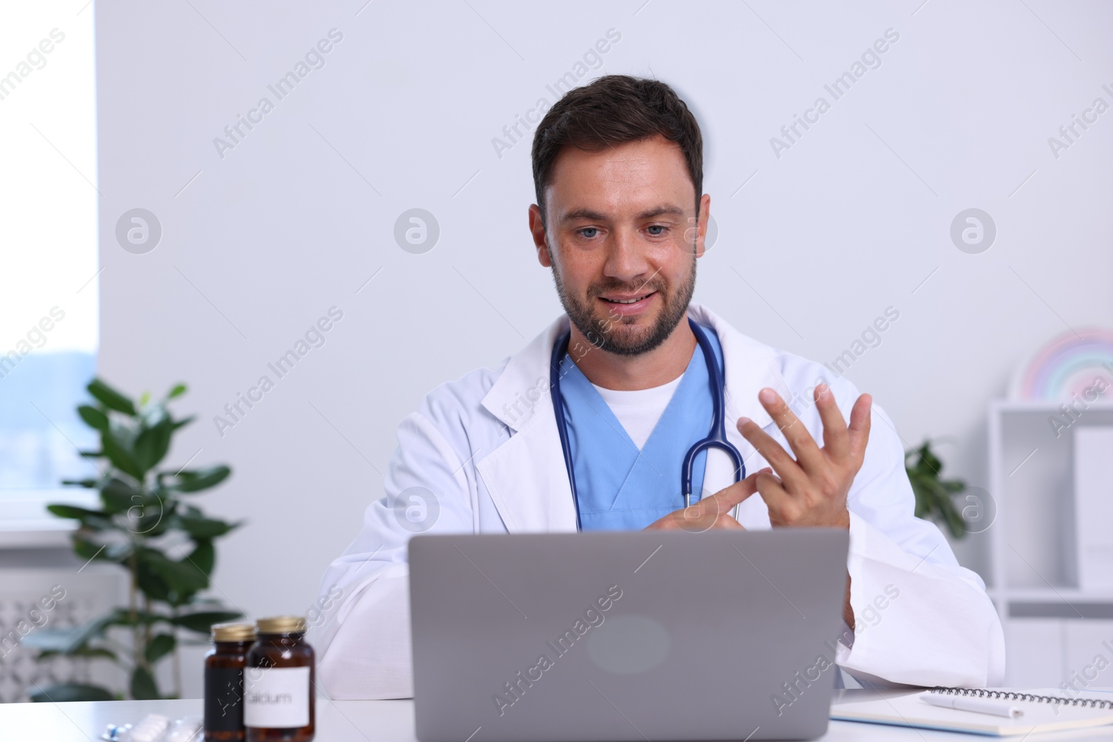 Photo of Pediatrician having video call with patient via laptop at desk in hospital