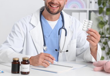 Photo of Pediatrician with pills and clipboard at desk in clinic, closeup