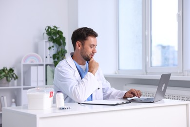 Photo of Pediatrician working on laptop at desk in hospital