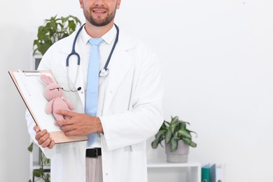 Photo of Pediatrician with clipboard and toy bunny in hospital. Space for text