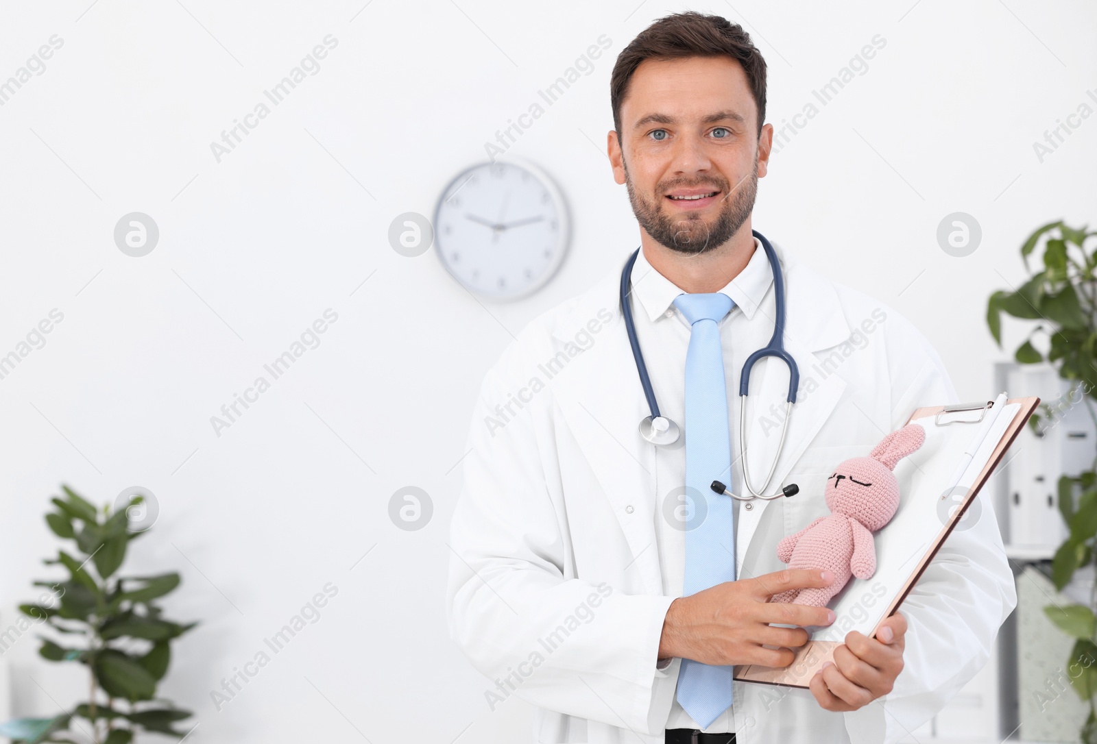 Photo of Pediatrician with clipboard and toy bunny in hospital. Space for text