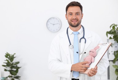 Photo of Pediatrician with clipboard and toy bunny in hospital. Space for text