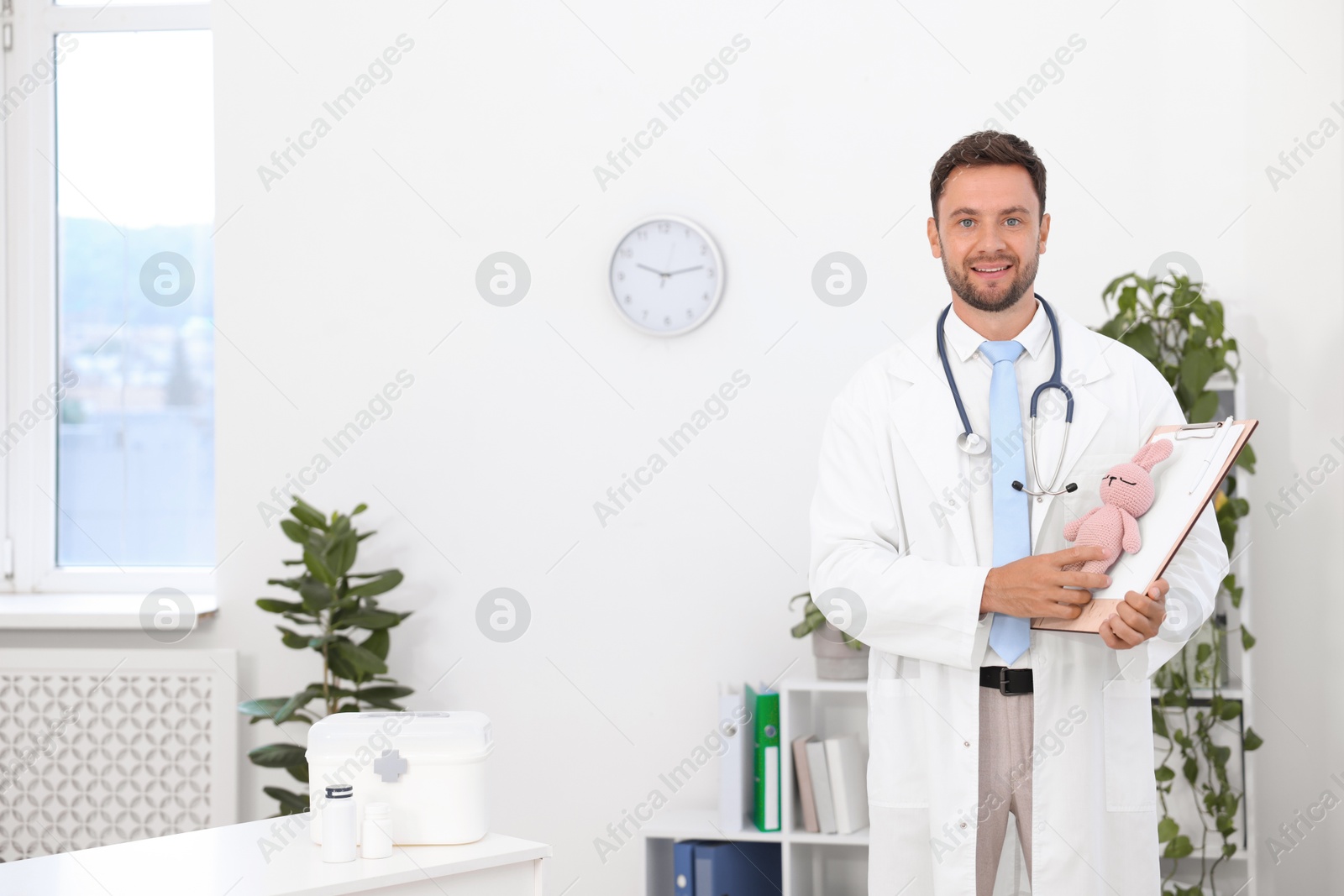 Photo of Pediatrician with clipboard and toy bunny in hospital. Space for text