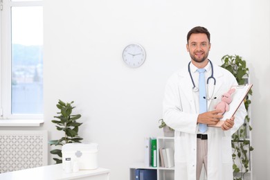 Photo of Pediatrician with clipboard and toy bunny in hospital. Space for text