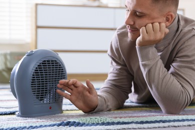 Photo of Young man near electric heater on floor at home