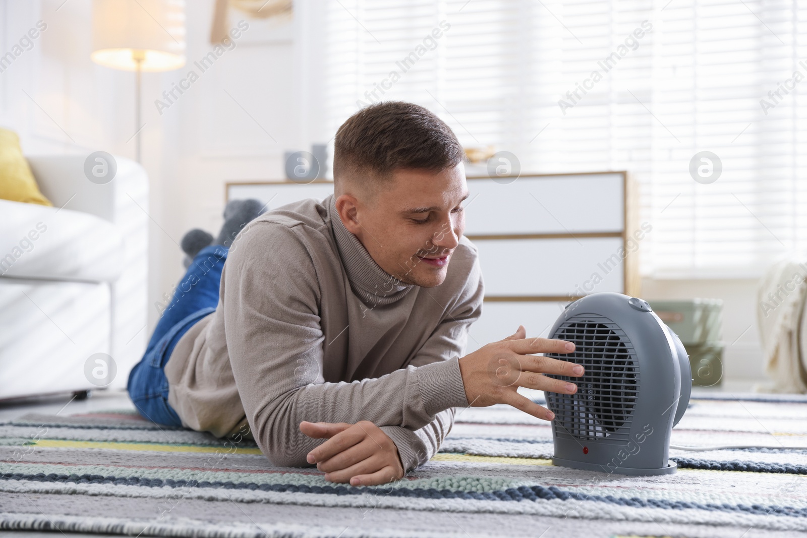 Photo of Young man near electric heater on floor at home