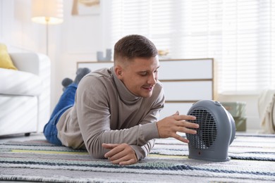 Photo of Young man near electric heater on floor at home
