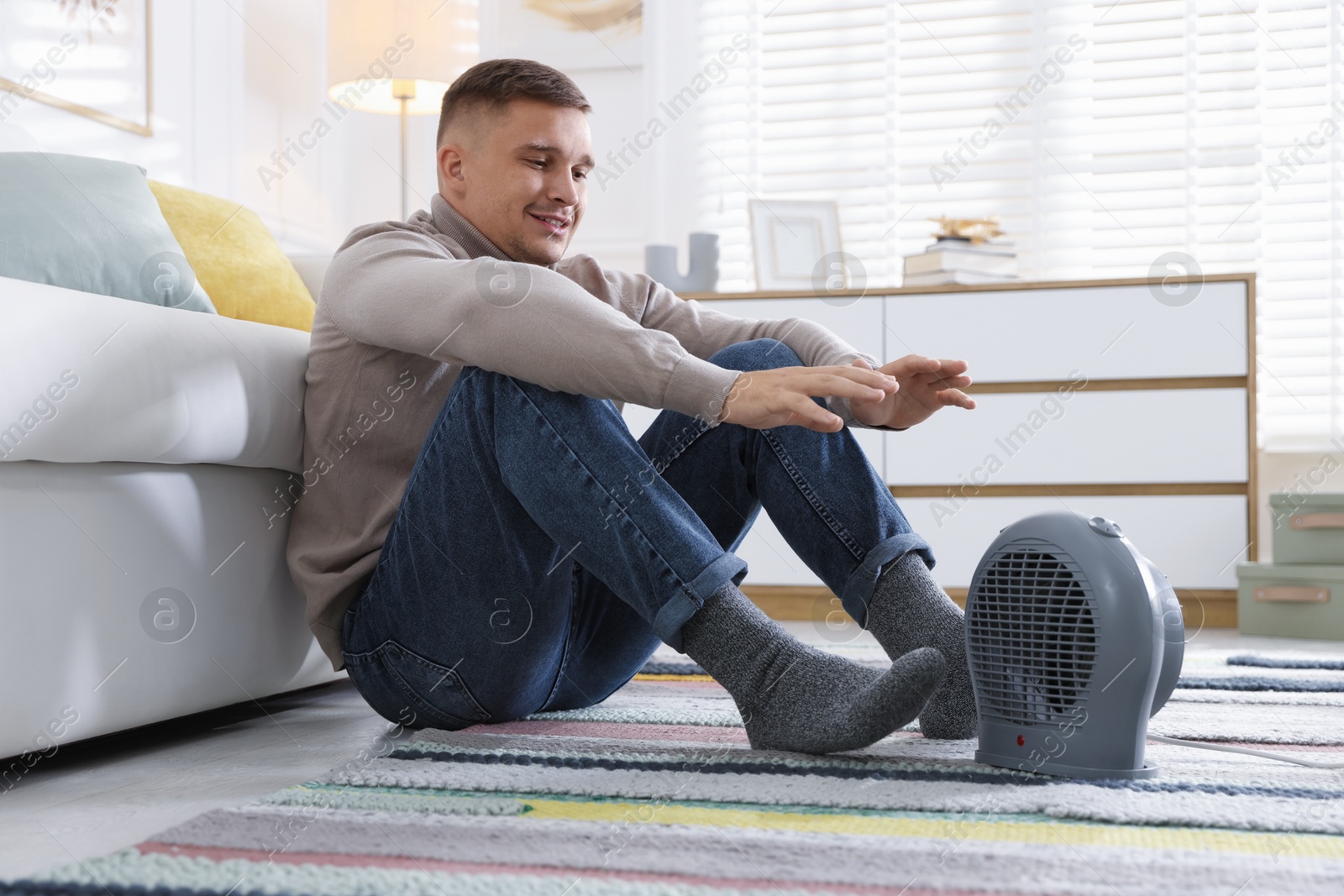 Photo of Young man near electric heater on floor at home